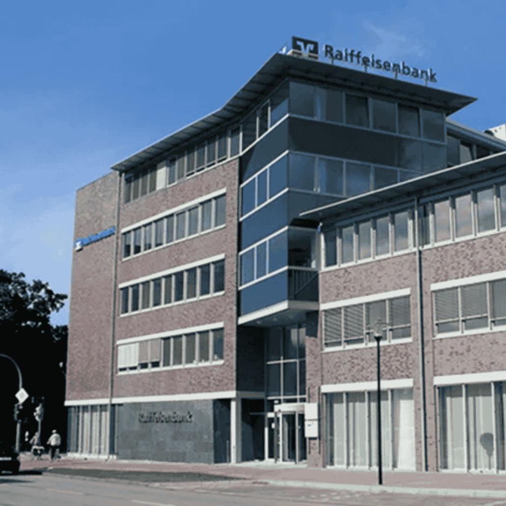 Karriere 7 Modernes Bürogebäude der Raiffeisenbank mit Glasfassade und rotem Klinker in städtischer Umgebung bei klarem Himmel.