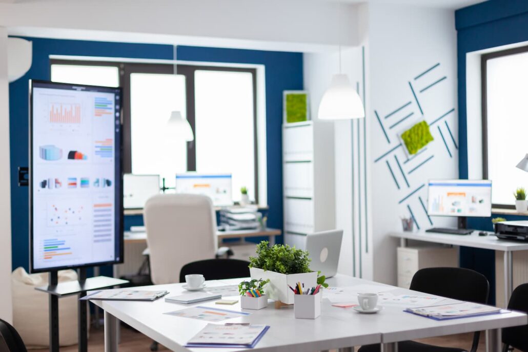 Karriere 9 Modern eingerichtetes Büro mit Schreibtischen, Computern, Flipchart mit Diagrammen und dekorativen Pflanzen.